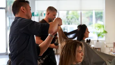 two women getting haircuts in salon by male hair stylists
