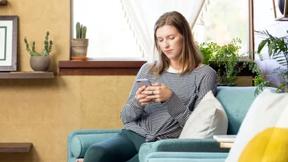 A person sitting on a chair, looking down at a phone in their hands