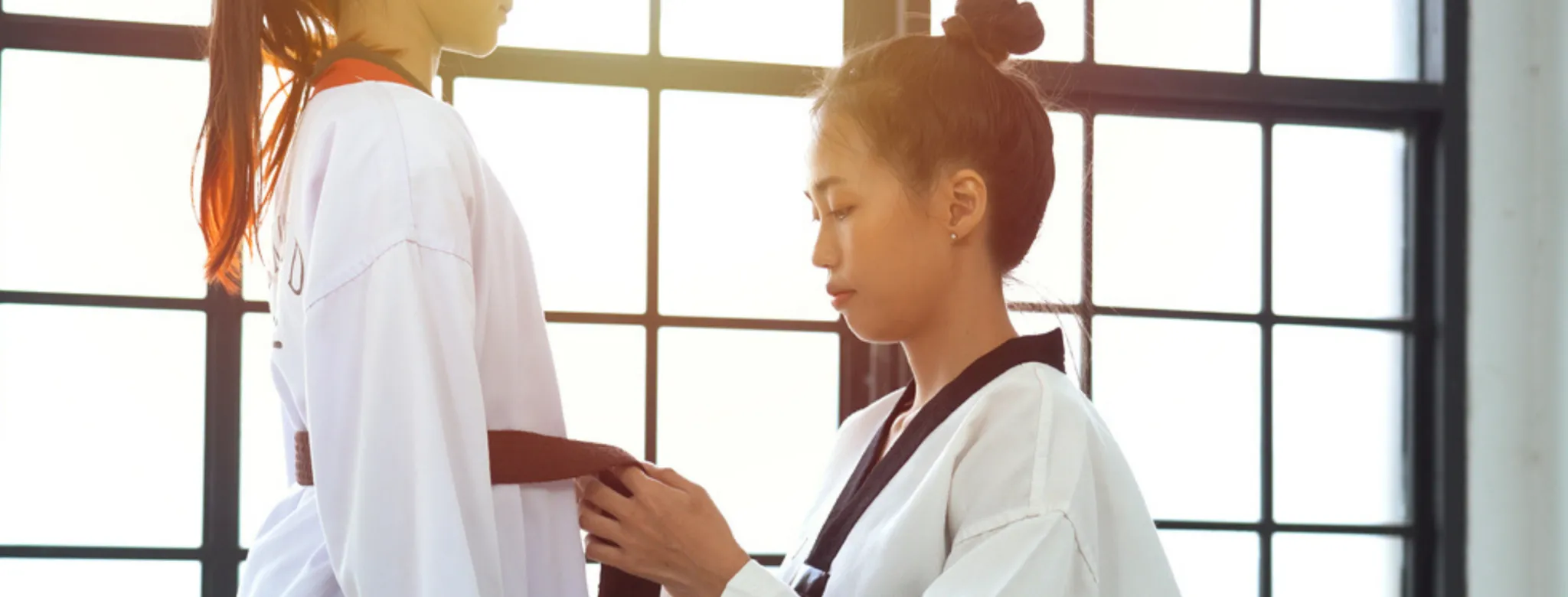 A martial arts instructor helps tie a student's black belt to prepare for Taekwondo