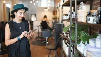 woman with hat on ipad in salon with products