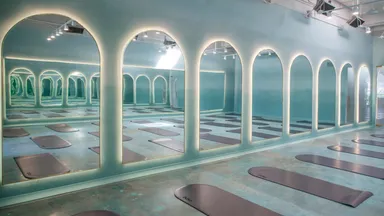 Empty room full of yoga mats with serene blue lighting and high arched floor to ceiling windows. 